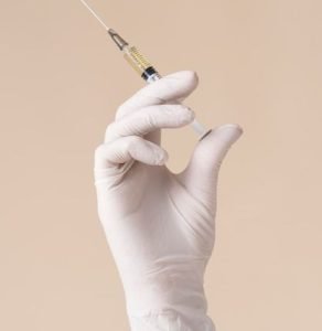 Hand with latex glove holding vaccine syringe